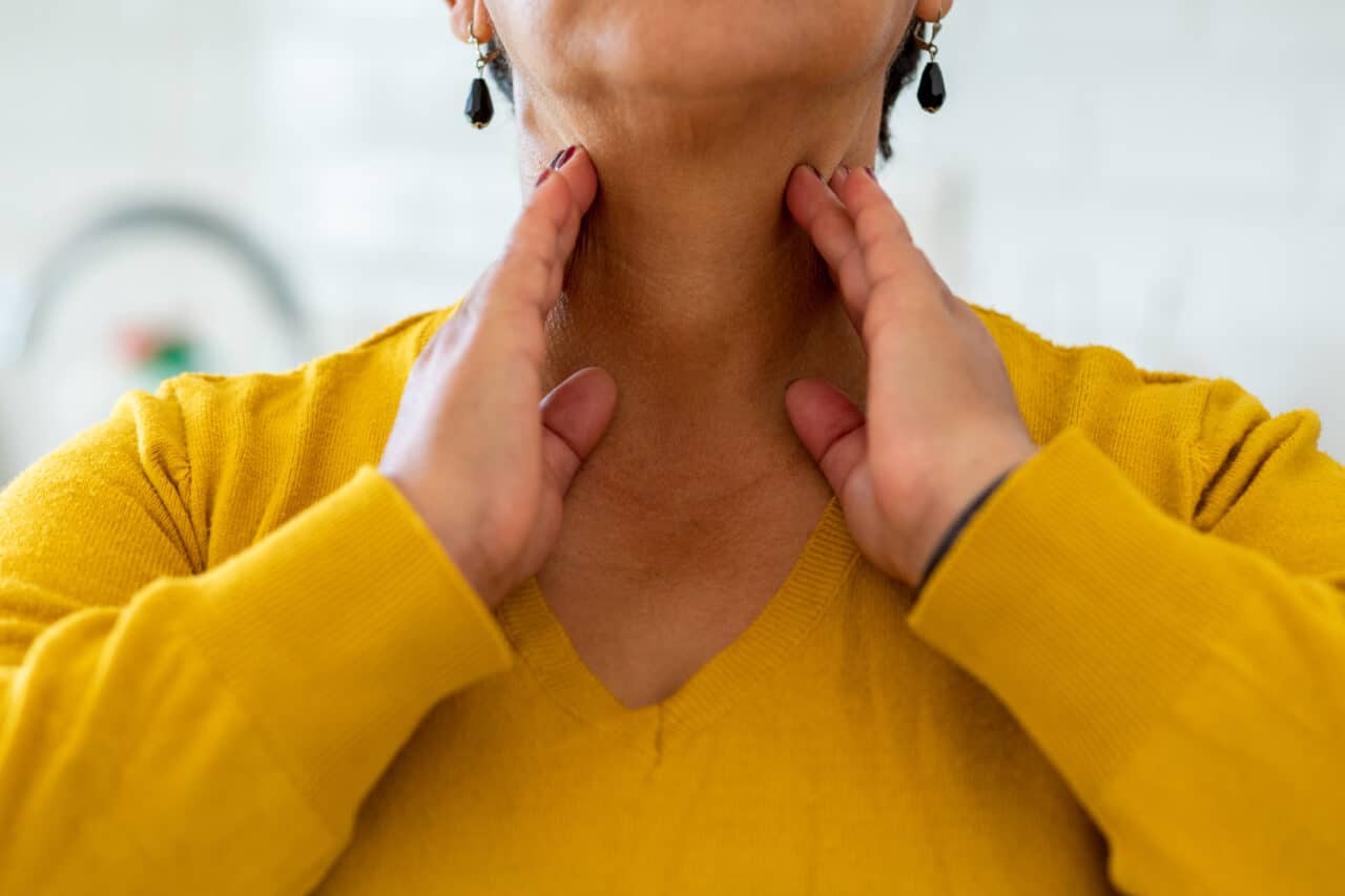 a woman in a yellow sweater touches her throat